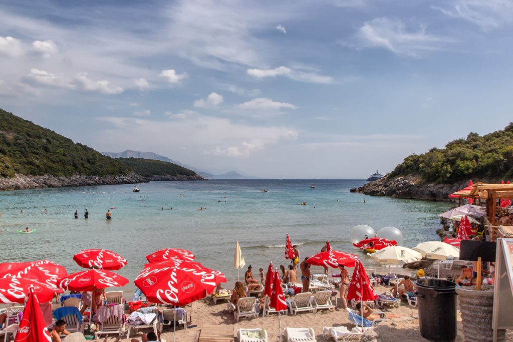 una spiaggia con ombrelloni rossi e un mare limpido, scorcio della spiaggia trsteno durante il viaggio in Montenegro