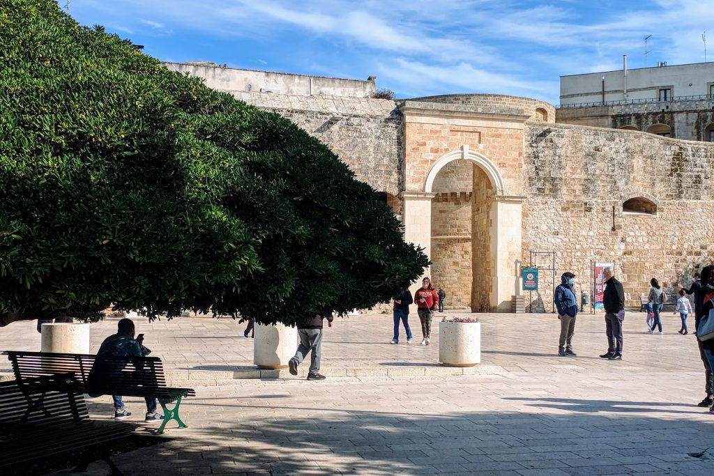 Vista della Porta Alfonsina di Otranto da sotto un albero con panchina